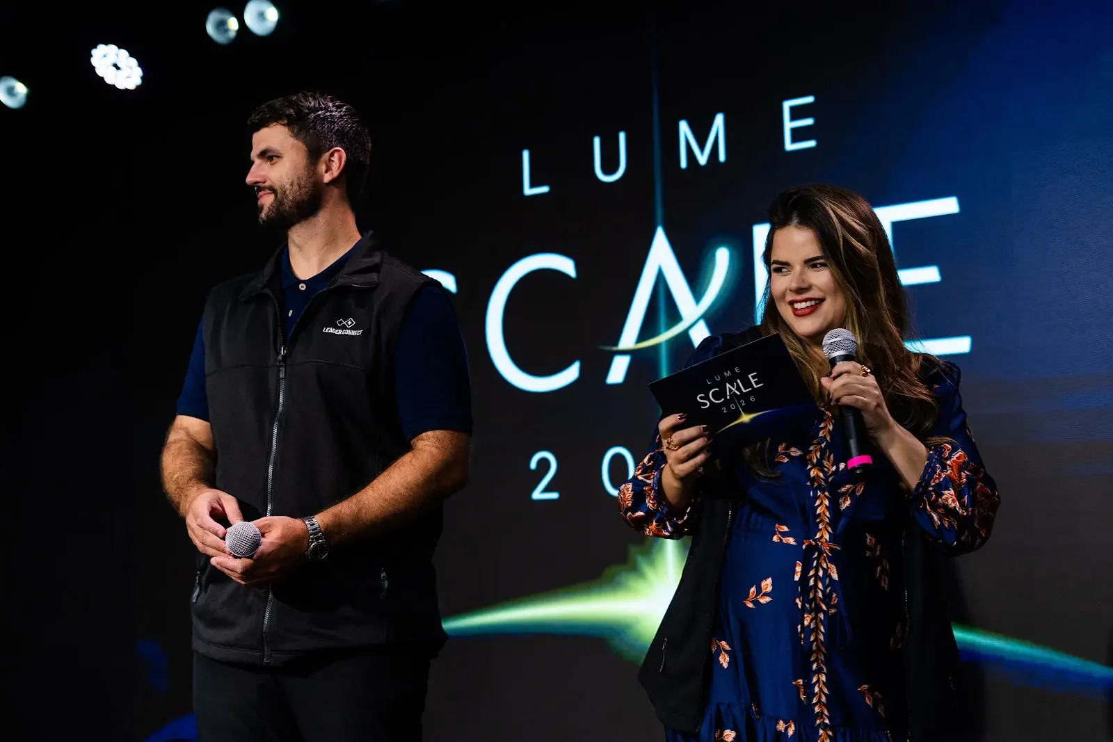 Amanda Antunes apresentando o Lume Scale no palco, com o microfone e o cartão do evento